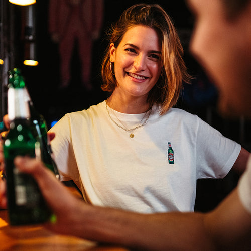 weibliches Model trägt weißes T-Shirt mit gestickter Becks Bierflasche in Bar Atmosphäre