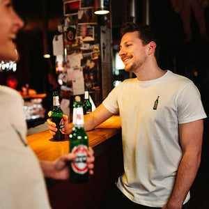 männliches Model trägt weißes T-Shirt mit gestickter Becks Bierflasche in Bar Atmosphäre