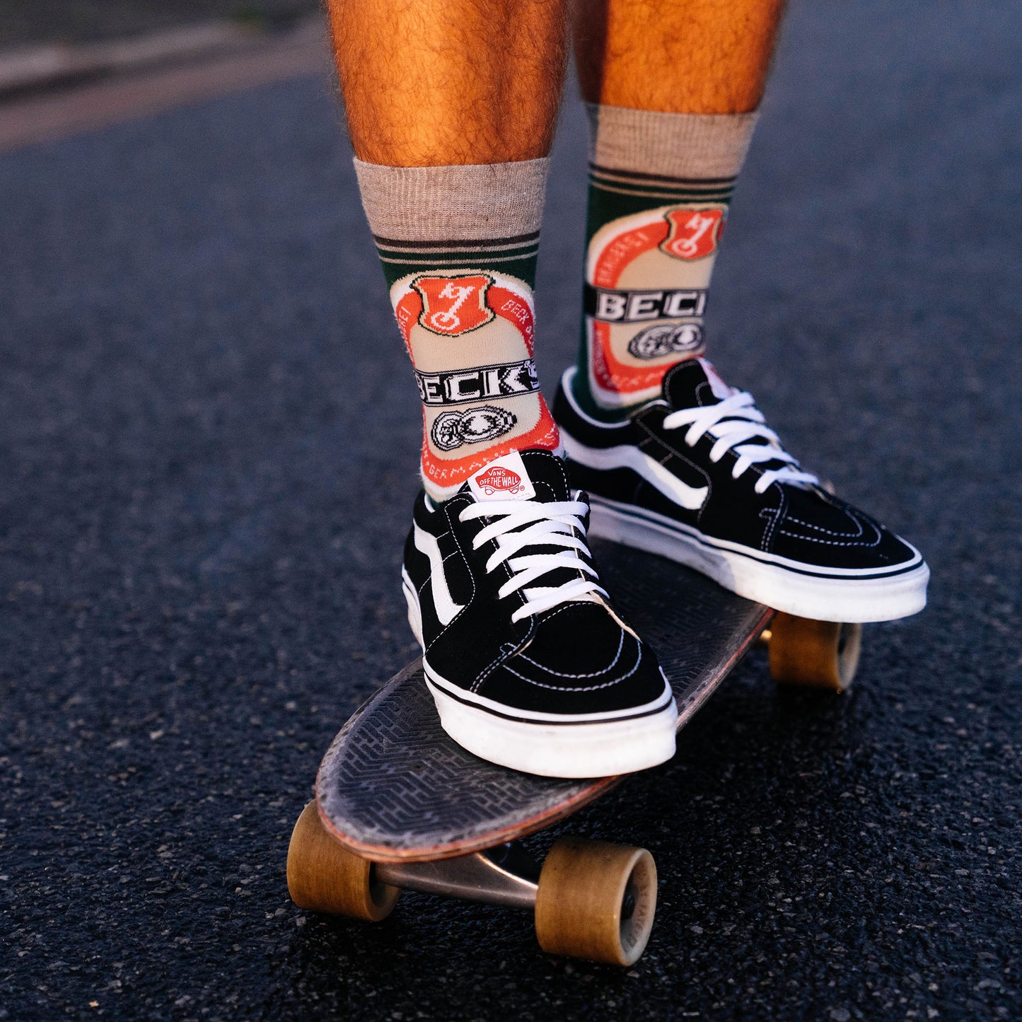 Füße in schwarzen Vans und hohen Becks Retro Socken auf einem Pennyboard